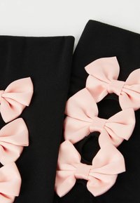 Tissu noir avec de petits nœuds en satin rose disposés en rangée, présentant des découpes circulaires. La texture est lisse et le design est ludique.