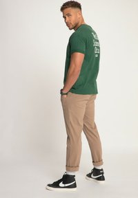 Camiseta de algodón verde con texto gráfico blanco en la parte posterior, pantalones beige ajustados y zapatillas negras altas con acentos blancos.