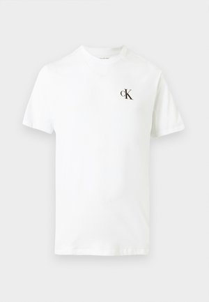T-shirt blanc à manches courtes avec un petit logo noir "cK" imprimé sur le côté gauche de la poitrine, fond uni.