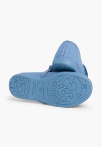 Zapatilla de lona azul con una suela de goma texturizada que presenta patrones de flores y corazones. El diseño incluye una puntera redonda y una correa de Velcro.
