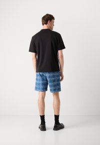 Svart kortermet skjorte, blå rutete shorts med hvite detaljer, svarte sokker og fottøy; minimalistisk design; monokromatiske og mønstrede elementer.