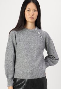 Grauer Strickpullover mit Rundhalsausschnitt, geripptem Saum und drei dekorativen Knöpfen an der Schulter. Sanfte Struktur und entspannter Schnitt.