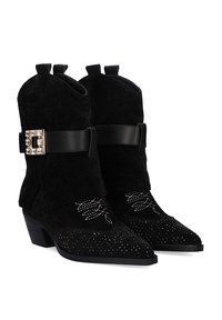 Botines de ante negro con puntera afilada, adornados con tachuelas plateadas y bordados florales, que cuentan con un cinturón decorativo negro en el tobillo.