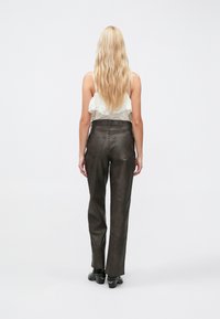 Pantalon marron foncé à jambes droites en tissu texturé avec poches arrière, porté avec un haut de couleur claire, vu de dos.