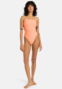 Maillot de bain une pièce côtelé pêche avec fines bretelles et décolleté carré, présentant une taille haute et une texture lisse.