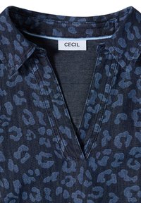 Chemise bleu foncé avec imprimé léopard abstrait bleu clair et col en V, affichant l'étiquette de la marque "Cecil" à l'encolure.