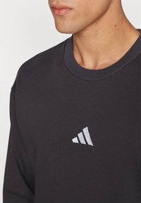 Sweatshirt preto com gola redonda feito de tecido misto de algodão. Apresenta um pequeno logo branco da Adidas no lado esquerdo do peito. Gola texturizada em costura canelada.