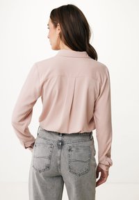 Lichtrozeblouse met lange mouwen, een kraag en een rugplooitje, gecombineerd met hoge taille, lichtgrijze denim jeans.