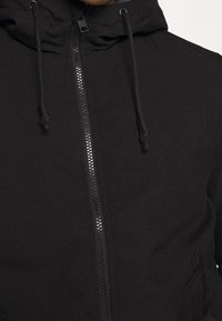 Černá mikina s kapucí na zip, vyrobená z texturované látky, se stažitelnou kapucí a zapínáním na zip, s diskrétními předními kapsami a bez viditelných log.