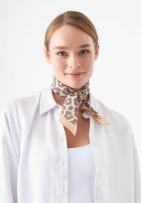 Écharpe à motifs léopard dans des teintes de marron et de beige, en tissu doux, nouée autour du cou, associée à une chemise blanche à boutons.