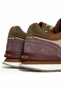 Une paire de baskets en daim brun et violet avec des semelles épaisses blanches et brunes, présentée de l'arrière sur un fond blanc.