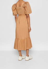 Beige puffärmad klänning med smockad byst och utsvängd nederkant. Modellen bär kraftiga vita sneakers, vilket ger en avslappnad stil.