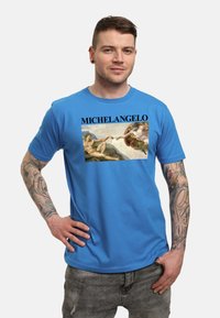 Camiseta de algodón azul con una impresión gráfica de la obra de Michelangelo, con texto en negrita que dice "MICHELANGELO" encima de la imagen.