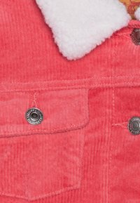 Manšestrová bunda v zářivé korálové barvě s bílým kožíškem na límci, přední kapsou na knoflík a po celé délce s žebrovanou strukturou.