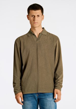 Langärmliges olivgrünes Polo-Shirt mit gerippter Textur, V-Ausschnitt und lockerer Passform, ergänzt durch Jeans.