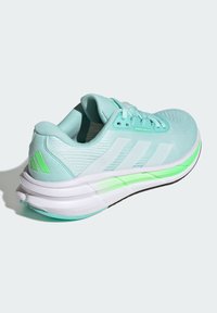Zapatilla de correr azul claro con acentos blancos, parte superior de malla texturizada, suela acolchada y un diseño distintivo de suela exterior en verde neón.
