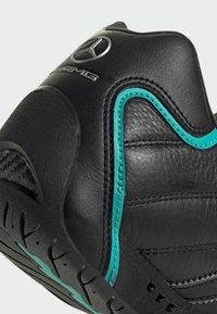 Black leather shoe with turquoise accent stitching, featuring a streamlined silhouette and textured sole. Logo visible on the heel.