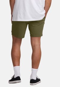 Pantalones cortos verde oliva con un corte recto, dos bolsillos laterales y dobladillo cosido. Combinados con zapatillas negras y calcetines blancos hasta el tobillo.