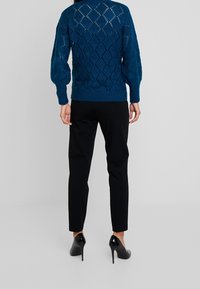 Turkusowy sweter z dzianiny w diamentowy wzór, z prążkowanymi mankietami i dołem. Połączony z wąskimi czarnymi spodniami i czarnymi szpilkami.