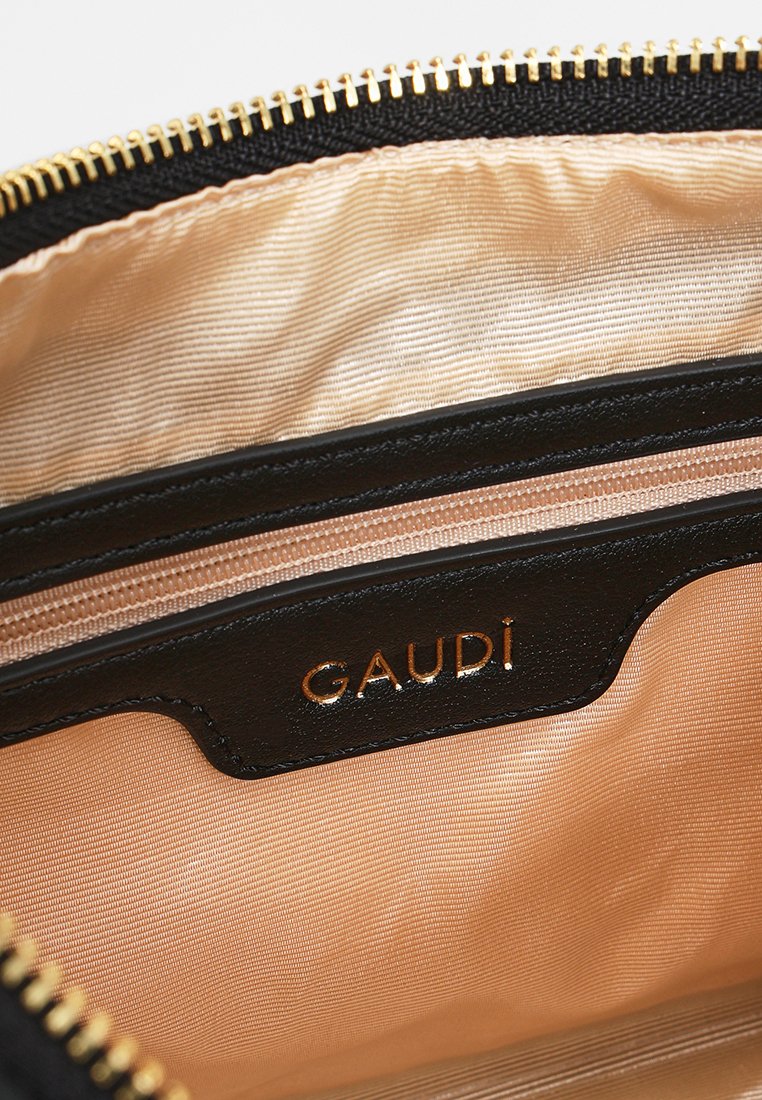 Interno di una borsa in pelle nera con una cerniera dorata, fodera in raso crema e un'etichetta in pelle nera impressa con la scritta "GAUDI".