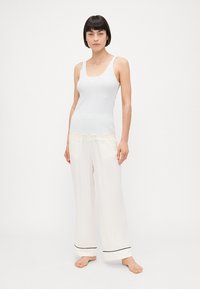 Camiseta de algodón a rayas con borde de encaje combinada con pantalones blancos sueltos con ribete negro. Textura suave, ajuste casual y ligera.