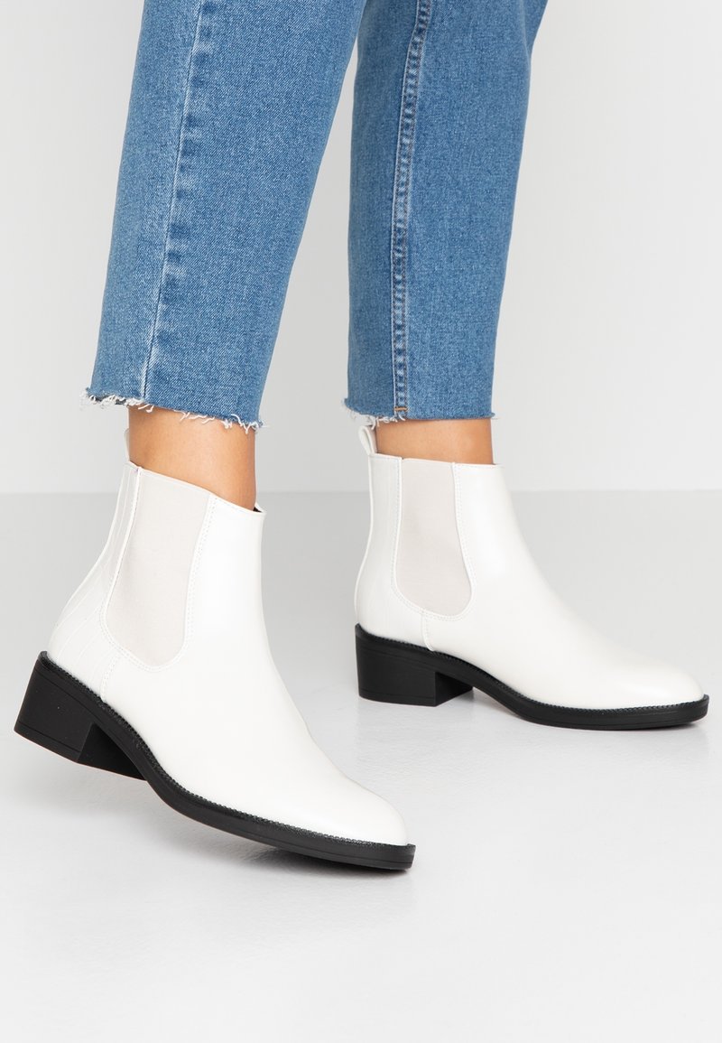 Bottes blanches en cuir à la cheville avec panneaux latéraux élastiques, talon léger et bout arrondi. Présente une finition texturée et une semelle noire.