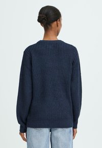 Marineblå striktrøje med en struktureret mønster, ribbede manchetter og kant, samt rund halsudskæring, set fra ryggen.
