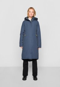 Langnavyblauwe jas met een ritssluiting aan de voorkant, een capuchon en zijzakken. Bevat gele ritsaccenten en een gladde, gestructureerde stof.