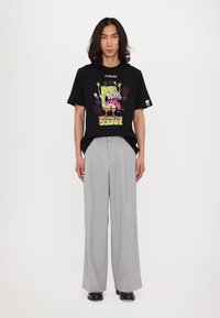 Black graphic t-shirt featuring a colorful SpongeBob design, paired with light gray wide-leg trousers and black shoes. Smooth fabric textures.