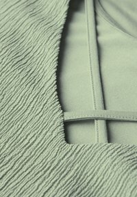Tessuto verde menta testurizzato con superficie ondulata, caratterizzato da un design con ritagli e accenti lisci. Il retro liscio completa il motivo.