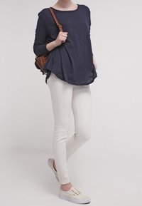 Granatowa bluzka z długim rękawem i okrągłym dekoltem, połączona z białymi obcisłymi dżinsami i jasnymi trampkami. Do stylizacji dołączona jest brązowa torebka typu crossbody.