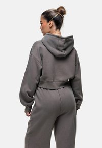 Felpa grigia corta realizzata in tessuto morbido, con un ampio cappuccio e spalle scese, abbinata a pantaloni tuta con vita elastica dello stesso colore.