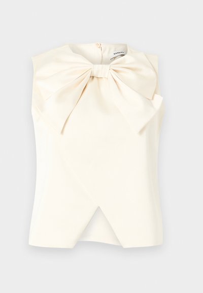 Blouse ivoire sans manches avec grand nœud à l'avant et ourlet asymétrique superposé, fermeture à boutons au niveau de l'encolure, fabriquée par Sandro.