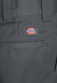 Pantalons de travail Dickies gris avec une texture tissée, poche arrière avec un patch logo et des détails de couture renforcés.
