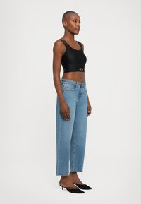Black crop top with wide straps, denim high-waisted trousers, and black low-heeled shoes. The outfit features a gold accent on the top.