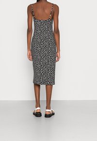 Svart figurnära klänning med vitt blommönster, spaghettiband och midi-längd. Bärs med vita sandaler med platå-sula.