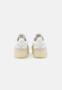 Bílé tenisky s robustní průhlednou podrážkou, semišovými detaily, polstrovaným límcem a logem Reebok na patě. Texturované materiály a hladký povrch.