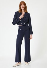 Mørkeblå dobbeltradet cropped blazer med sølvknapper, parret med højtaljede wide-leg bukser i samme farve og bløde materiale.