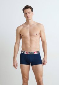 Boxers en jersey bleu marine pour hommes avec une ceinture élastique marquée de couleurs noire, rouge et blanche ; tissu lisse et design ajusté.