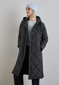 Prošívaný černý dlouhý kabát s kapucí, s patentkami a bočními kapsami. Doplněný světle modrou pletenou šálou.