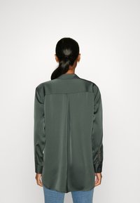 Dark green satin shirt with a classic collar, long sleeves, and a back pleat. Designed with a curved hem and buttoned cuffs.