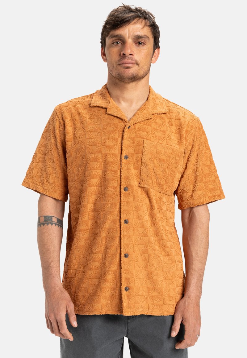 Short-sleeve, terry cloth shirt in burnt orange with a textured pattern of squares and sunburst designs; single chest pocket and black buttons.