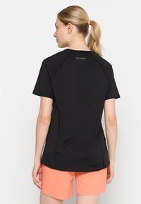 Svart kortärmad idrottströja med en slät textur, med raglanärmar och en liten logotyp på baksidan. Kombinerad med korallfärgade shorts.