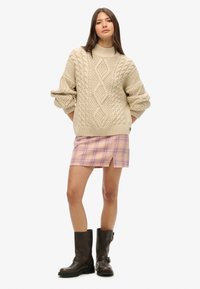 Beżowy sweter z dzianiny w romby, ze ściągaczem przy szyi i mankietach, w połączeniu z różową mini spódniczką w kratkę z bocznym rozcięciem oraz brązowymi botkami sięgającymi kostki.