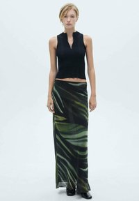 Zwarte geribbelde crop top met een subtiele rits, gecombineerd met een vloeiende maxi rok met een groen en zwart bladerenpatroon. Glad textuur, aansluitende silhouet.