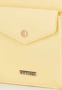 Portefeuille en simili cuir jaune avec un rabat géométrique, une fermeture pression dorée, et un accent métallique du logo de la marque. Détails de couture minimalistes.