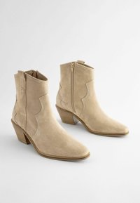 Beiga mockaskinnsanklar med spetsig tå, västernstil med scalloped-design och dragkedja på sidan. Har en staplad klack för stabilitet.