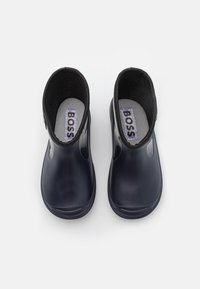 Une paire de bottes de pluie en caoutchouc bleu marine avec des finitions noires et des semelles intérieures grises portant la marque "BOSS", vues de dessus sur un fond blanc.