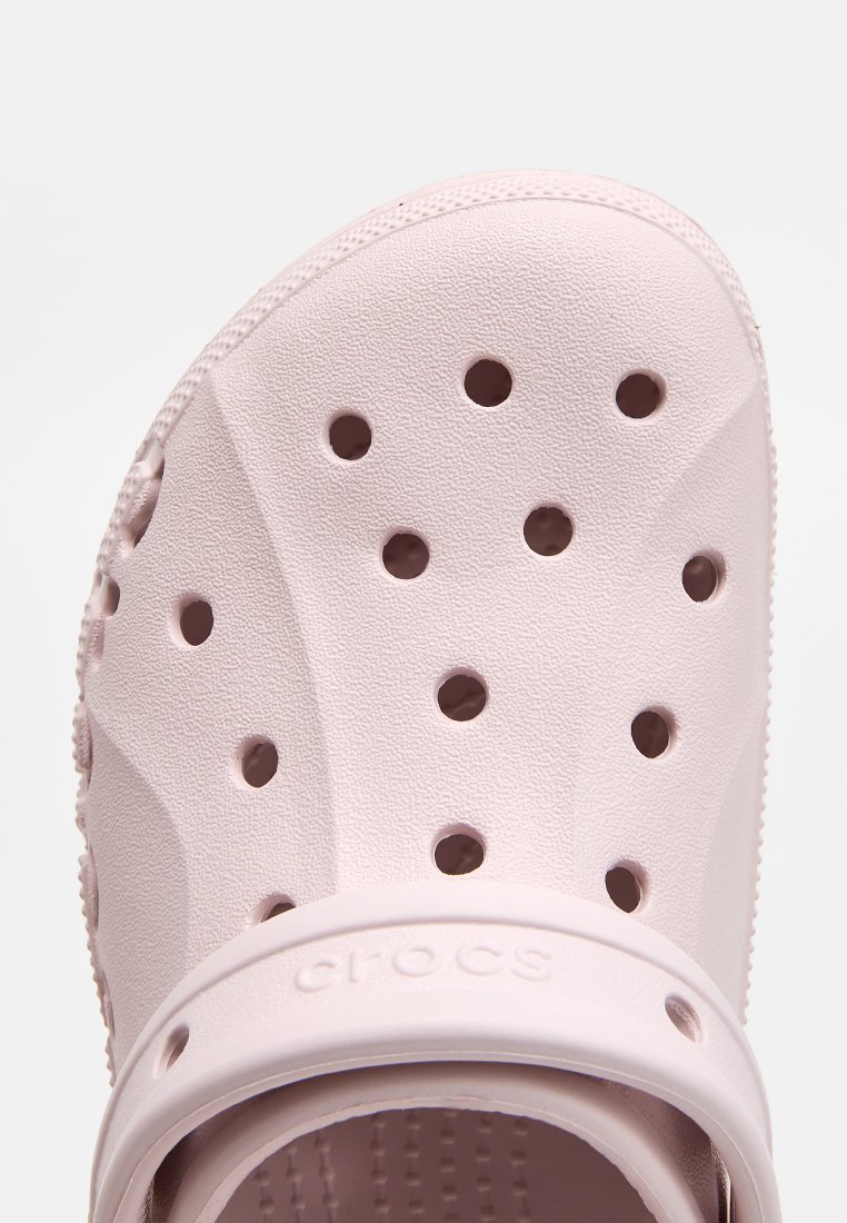 Crocs de color rosa claro con una superficie texturizada, múltiples agujeros de ventilación y una correa gruesa con el nombre de la marca grabado.