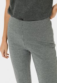 Juodos ir baltos houndstooth rašto kelnės su aukštu liemeniu, liekna prigludimu ir lygia tekstūra; derinamos su pilku trumpomis rankovėmis viršutiniu drabužiu.